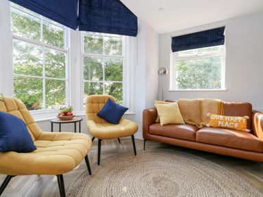 A living room with two yellow chairs with blue cushions a brown sofa with pillows and a blanket next to windows with blue blinds at Flat 6 Thornlow Heights in Weymouth