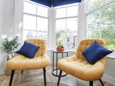 Two yellow chairs with blue pillows and a small round table with fruit between windows at Flat 6 Thornlow Heights in Weymouth