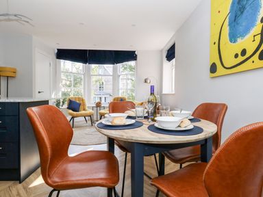 A dining area with a round table set for four and brown chairs near windows with yellow armchairs at Flat 6 Thornlow Heights Weymouth
