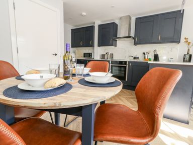 A kitchen with dark cabinets a round wooden dining table set with bowls glasses and bread at Flat 6 Thornlow Heights Weymouth