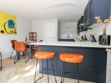 A kitchen and dining area with orange chairs and stools a marble countertop and a yellow and blue painting on the wall at Flat 6 Thornlow Heights in Weymouth