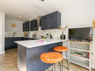 A kitchen with dark cabinets marble countertops orange bar stools and a TV on a white stand at Flat 6 Thornlow Heights in Weymouth