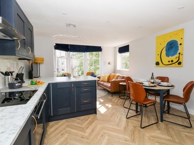 A kitchen and dining area with dark blue cabinets a round dining table with four brown chairs and a sitting area with a brown sofa at Flat 6 Thornlow Heights in Weymouth