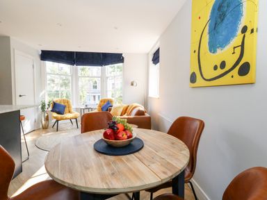 A dining area with a round wooden table and brown chairs and a living space with yellow chairs and a sofa at Flat 6 Thornlow Heights in Weymouth