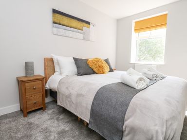 A bedroom with a bed with rolled towels on it a wooden bedside table and a window with an orange blind at Flat 6 Thornlow Heights in Weymouth