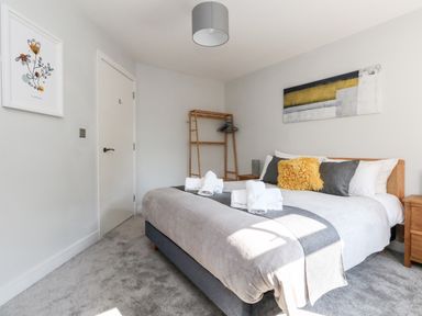 A bedroom with a bed with pillows and folded towels a wooden clothes rack and abstract painting on the wall at Flat 6 Thornlow Heights Weymouth