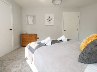 A bedroom with a double bed with rolled towels and pillows next to a wooden chest of drawers with a decorative object a mirror and framed artwork on the wall at Flat 6 Thornlow Heights Weymouth