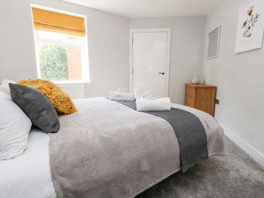 A bedroom with a bed grey and white bedding pillows and folded towels a window with an orange blind and a wooden chest of drawers on the right wall at Flat 6 Thornlow Heights Weymouth