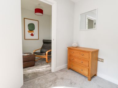 A small room with a wooden chest of drawers and a wall mirror next to a room with a black chair and brown ottoman at Flat 6 Thornlow Heights Weymouth