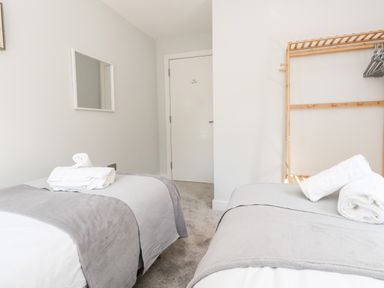 A bedroom with two single beds with gray blankets and white towels a wooden clothes rack with hangers and a white door at Flat 6 Thornlow Heights in Weymouth