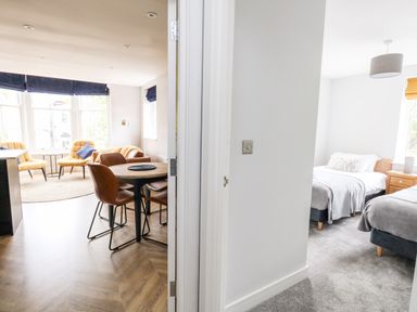 A dining area with a round table and chairs next to a living area with yellow chairs and a bedroom with two single beds at Flat 6 Thornlow Heights Weymouth