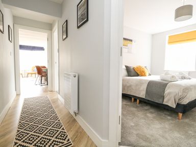 A hallway with a patterned runner rug leading to a dining area and a bedroom with a bed and rolled towels at Flat 6 Thornlow Heights in Weymouth