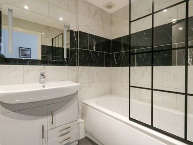 A bathroom with a sink vanity and a bathtub with a glass partition at Flat 6 Thornlow Heights Weymouth