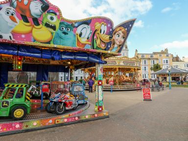 An outdoor amusement area with children's rides including a merry-go-round and cartoon-themed vehicles in Weymouth