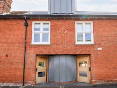 A brick building facade with two wooden doors and white-framed windows at The Old Gymnasium in Southwold
