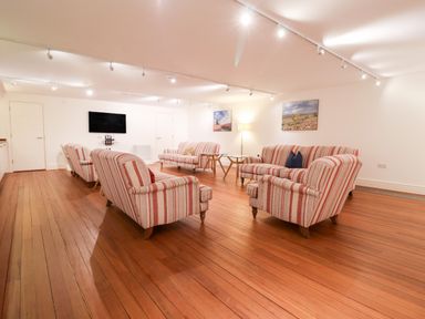 A sitting room with striped armchairs and two sofas wooden floor and TV on wall at The Old Gymnasium in Southwold