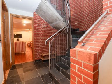 A hallway with black tiled floor red brick walls and a staircase with metal handrails at The Old Gymnasium in Southwold