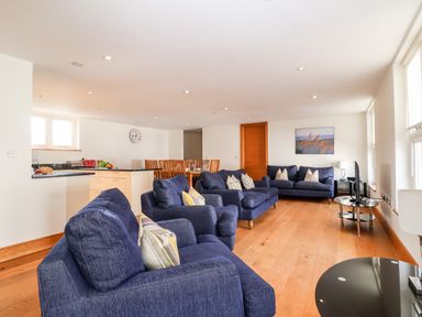A living room with blue sofas and wooden dining table near a kitchen at The Old Gymnasium in Southwold