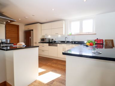 A kitchen with black countertops white cabinets wooden floor and various kitchen appliances at The Old Gymnasium Southwold