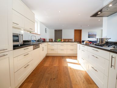 A modern kitchen with white cabinets black countertops wooden floor and dining table at The Old Gymnasium in Southwold