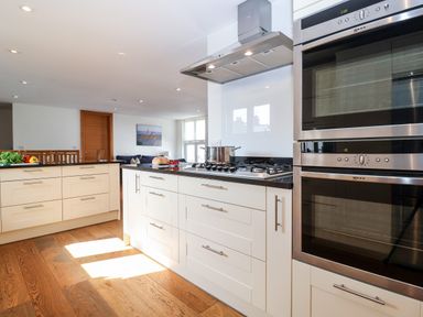 A kitchen with white cabinets wooden floor double ovens and a cooking pot on the stove at The Old Gymnasium Southwold
