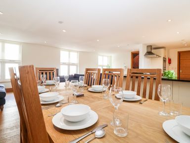 A dining table set with white bowls plates glasses and cutlery in a room with wooden chairs and windows at The Old Gymnasium in Southwold