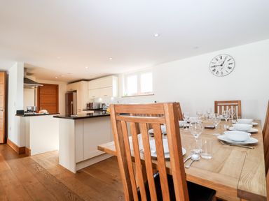 A dining area with a wooden table set with plates and glasses next to a kitchen with white cabinets and black countertops at The Old Gymnasium in Southwold