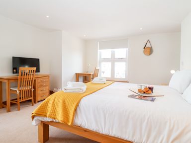 A bedroom with a bed, two wooden desks with chairs, a TV, and a window at The Old Gymnasium in Southwold