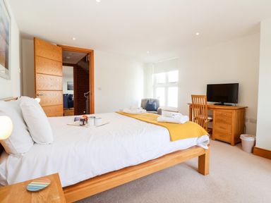 A bedroom with a wooden bed a desk and chair a TV an armchair and a window at The Old Gymnasium in Southwold