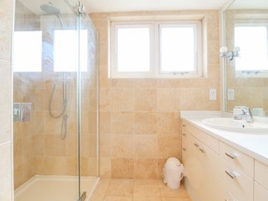 A bathroom with a glass shower enclosure a sink with a countertop and cabinets and a small trash bin at The Old Gymnasium in Southwold
