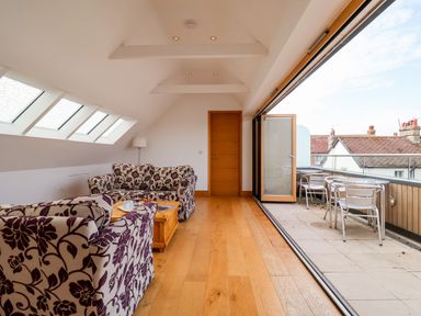 A living room with patterned armchairs a coffee table wooden floor and a balcony with outdoor furniture at The Old Gymnasium in Southwold