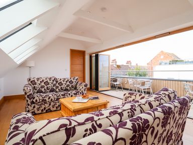 A living area with floral patterned sofas, a wooden coffee table, folding glass doors opening to a balcony with metal chairs at The Old Gymnasium in Southwold