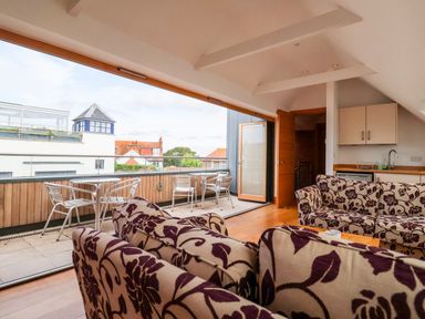A living area with floral patterned sofas and a balcony with metal tables and chairs at The Old Gymnasium in Southwold