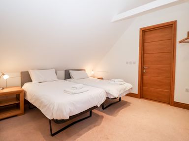 A bedroom with two single beds bedside tables with lamps and a wooden door at The Old Gymnasium in Southwold