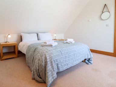 A bedroom with a double bed with white pillows and gray blanket and two wooden bedside tables with lamps at The Old Gymnasium in Southwold