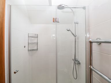 A shower area with a glass door a wall-mounted showerhead and a metal shower caddy at The Old Gymnasium in Southwold