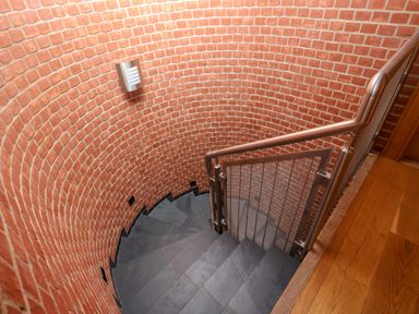 A spiral staircase with dark stone steps and brick walls at The Old Gymnasium in Southwold