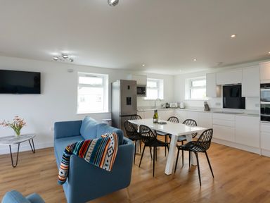 An open-plan kitchen and living area with a blue sofa a white dining table with black chairs and kitchen appliances at Treen St Ives