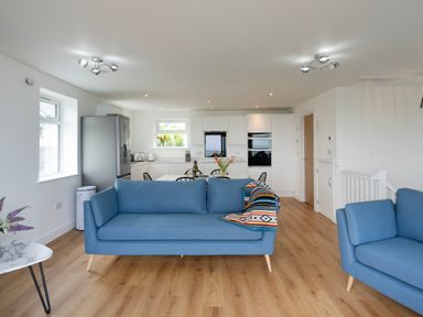 A living room with blue sofas and a kitchen with white cabinets in the background at Treen in St Ives