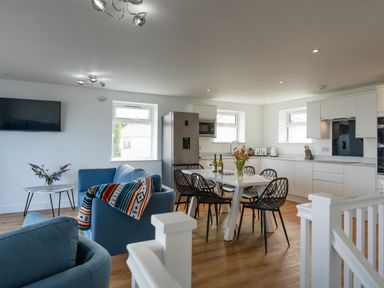 A kitchen and dining area with a white table and black chairs next to a blue sofa and armchair at Treen in St Ives