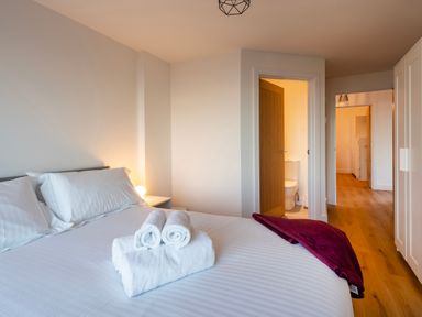 A bedroom with a bed with white linens and towels a bedside table a door leading to a bathroom and a hallway at Treen in St Ives