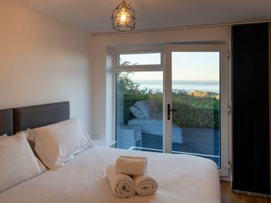 A bedroom with a bed and rolled towels on it and a glass door showing a view of the sea at Treen in St Ives