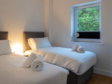 A bedroom with two single beds and rolled towels on the beds next to a window showing greenery at Treen in St Ives