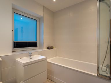 A bathroom with a bathtub a sink with cabinet a window and a shower enclosure at Treen in St Ives