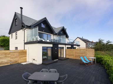 A house with a large patio with a table and chairs and two blue lounge chairs at Treen in St Ives