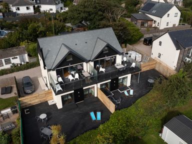 A two-story house with balconies and outdoor seating on a wooden deck surrounded by greenery at Treen in St Ives