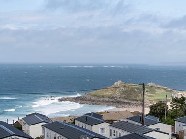 A coastal view of the ocean with waves and rocky shoreline near houses at Treen in St Ives