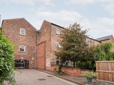 A brick building with multiple windows a gated entrance and a tree with red berries at 6 Granary Court in York