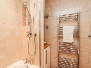 A bathroom with a shower, bathtub, chrome towel radiator with a white towel, and a cabinet with wooden countertop at 6 Granary Court in York