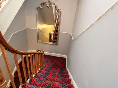 A staircase with wooden banister and red patterned carpet with a large decorative mirror on the wall at The Esplanade in Weymouth